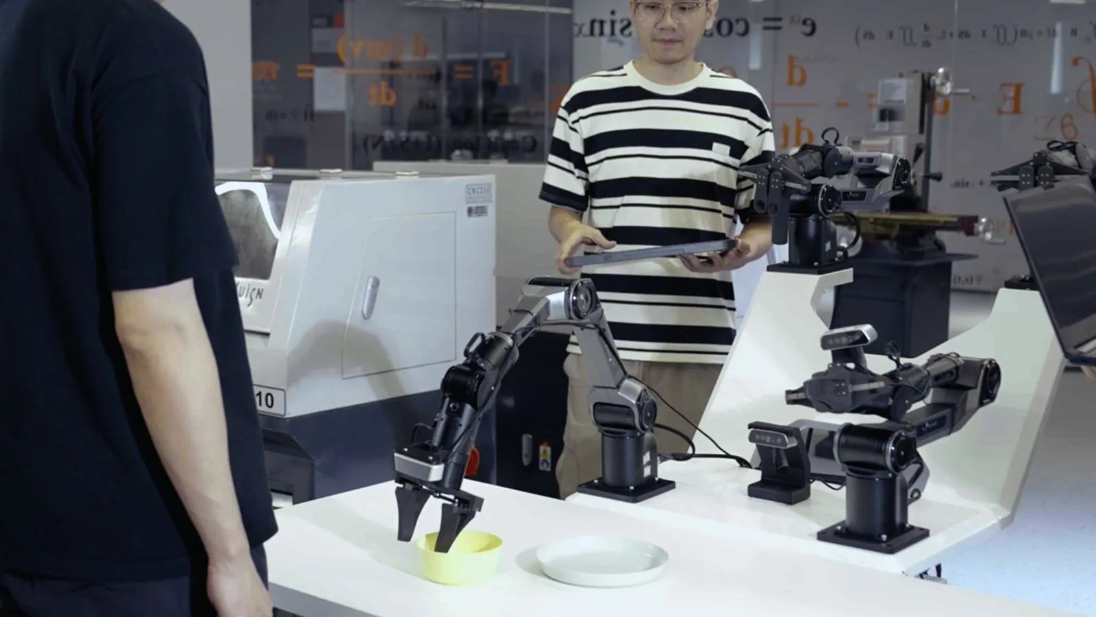 Operator z tabletem steruje ramieniem PiPER w laboratorium dydaktycznym, obok drugie ramię z chwytakiem